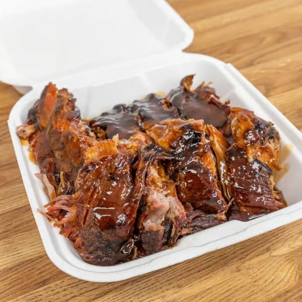Dad's BBQ pulled pork, drenched in rich barbecue sauce, in a white takeout container.