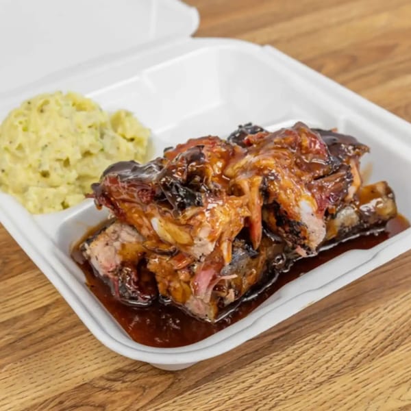 Dad's BBQ ribs with rich sauce and a side of mashed potatoes in a white takeout container.