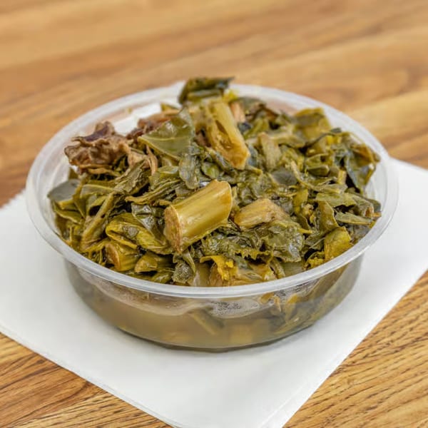 A clear plastic container filled with dark green collard greens, resting on a white napkin.