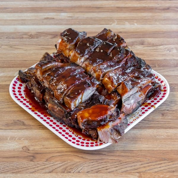 Dad's BBQ ribs, generously coated in a rich, dark barbecue sauce on a white and red polka dot plate.
